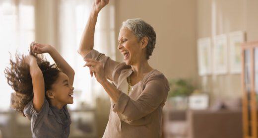 A senior woman laughing and dancing with her granddaughter.