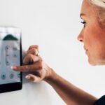 blonde middle-aged woman looking at thermostat and adjusting temperature lower