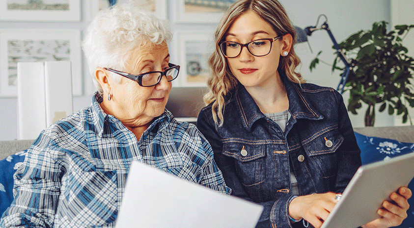 A young woman and a senior woman sit together and are reviewing documents