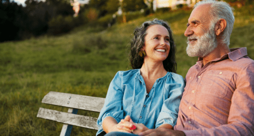 Retired couple sitting and smiling on bench together