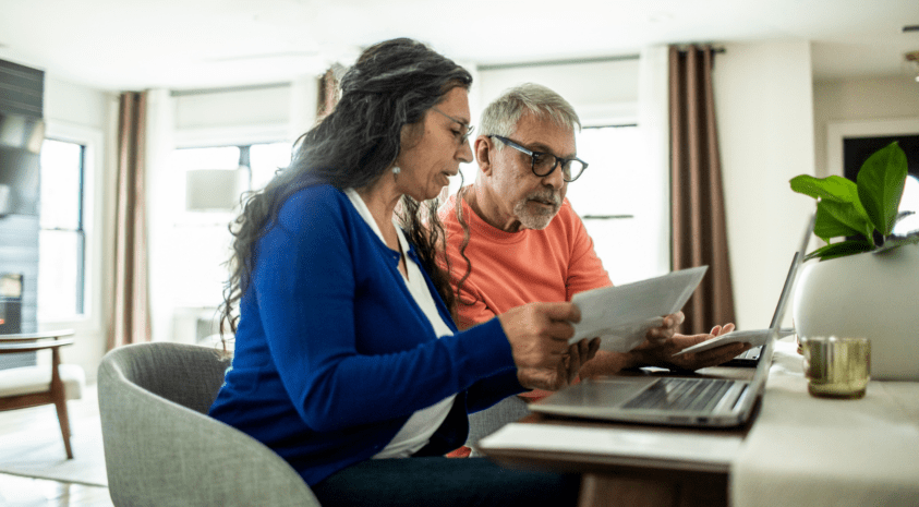 Older couple sitting at a laptop and looking at paperwork