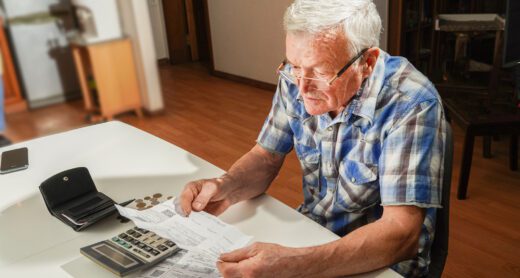 Senior man sitting at a table going over paperwork and using a calculator.