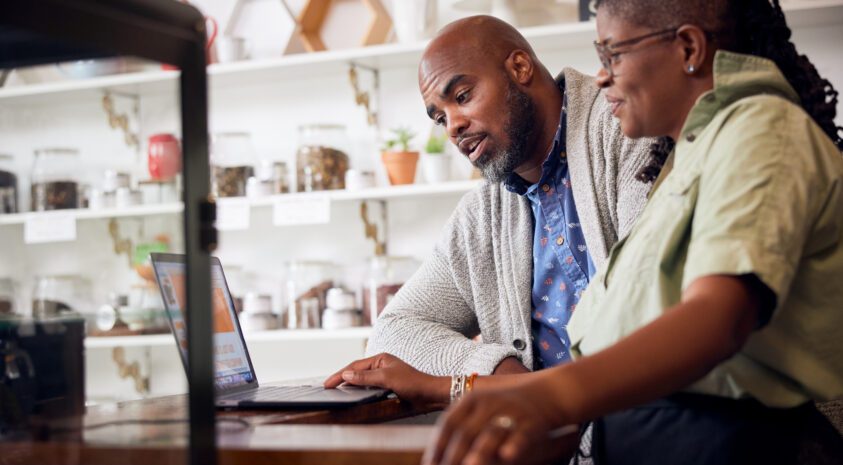 Two Black business owners leaning on a counter and looking at a laptop together.