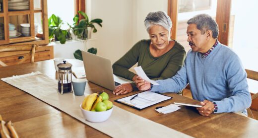Older couple managing their paperwork together at home at the dining room table.
