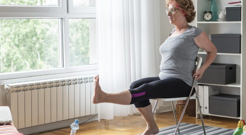 Senior woman stretching her leg while sitting on chair at home.
