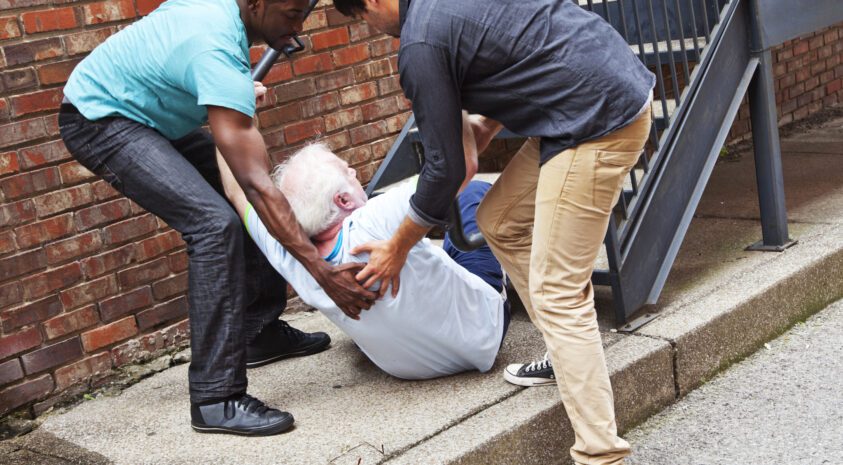 A senior man has fallen down the stairs backwards and two young men help him up