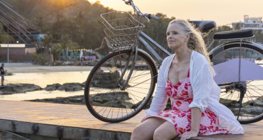 Senior woman pauses with bicycle on pier as sun rises over distant mountains