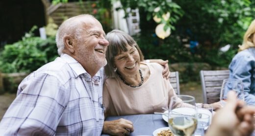 An older couple embracing and smiling while enjoying an outdoor meal with the family in a courtyard.