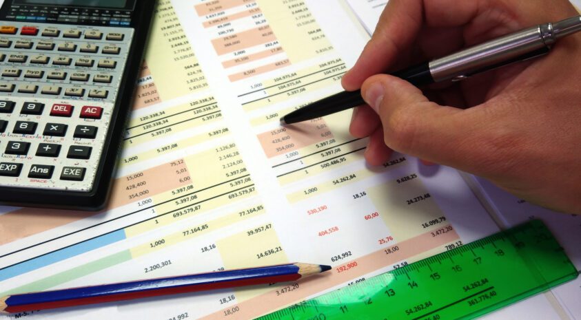 Close up of a person's hand holding a pen going over financial statements.