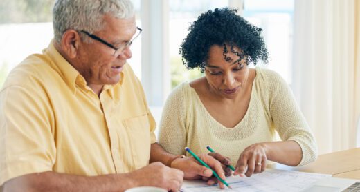 Older couple work on financial documents at table in their home.