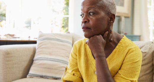 Older woman looking worried and stressed while sitting on her couch.