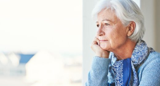 Older woman looking slightly sad gazing out of her window.