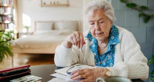 Widowed woman sits at her table with financial information looking concerned.