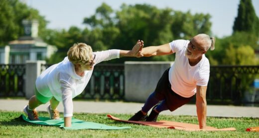 An older man and woman high-five while in plank pose.