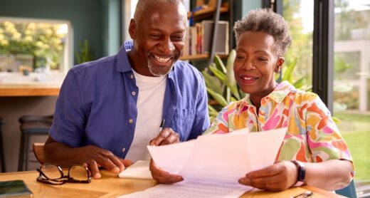 Senior couple smiles while looking at papers at their kitchen table.