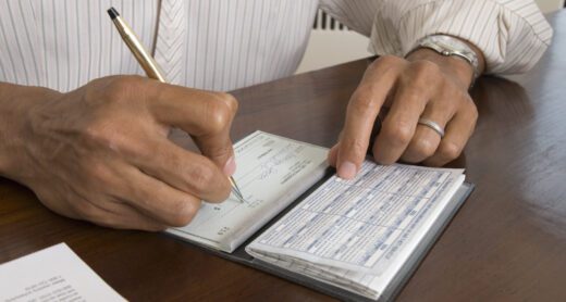 Close up of man's hands writing check with a pen.