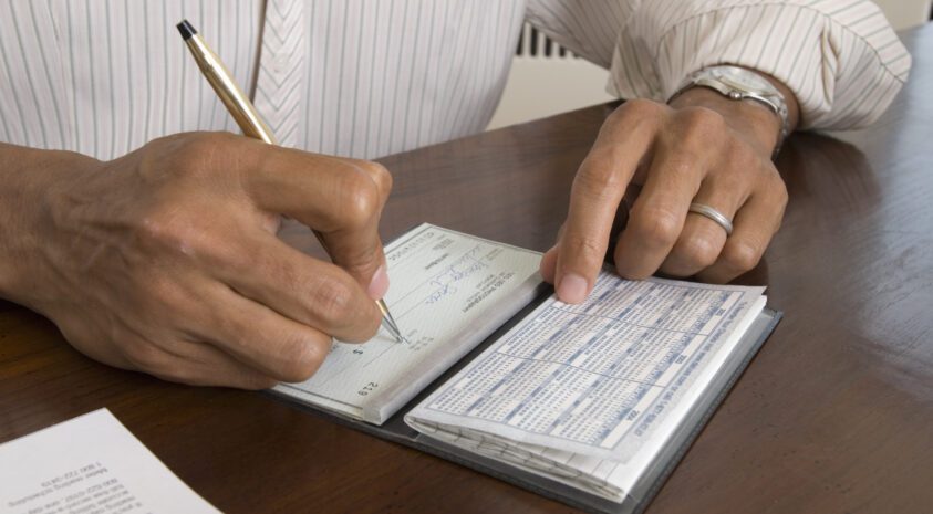 Close up of man's hands writing check with a pen.
