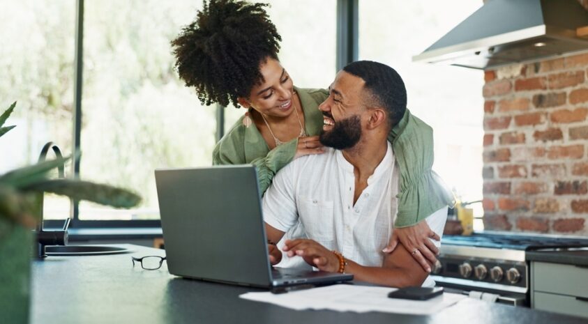 A couple embraces while using a laptop.