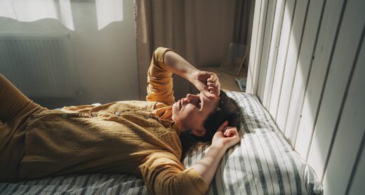 Woman lies on bed with her hand over her head feeling fatigued.