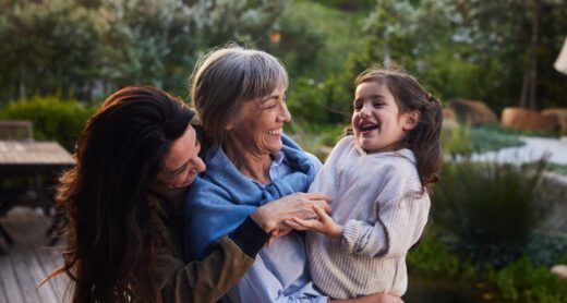 Little girl laughing while standing outdoors with her grandmother and mom.