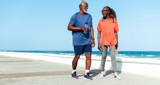 An older couple walks on a beachside promenade.