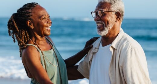 An older couple embraces on a beach.