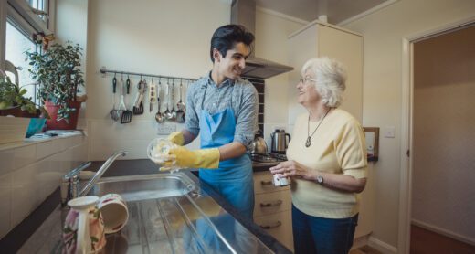 Young man helps older woman with washing dishes in her kitchen.