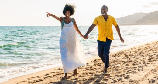 A couple holds hands on a beach.