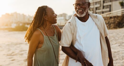 Happy older couple walking along beach smiling.