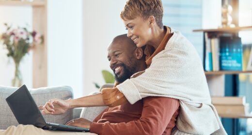 A couple sits on a couch while using a laptop.