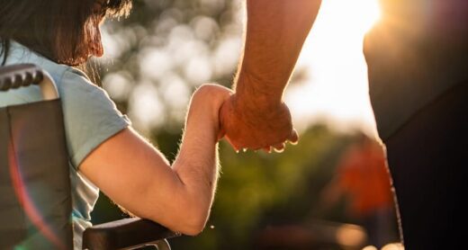 A parent holds hands with their adult child with disabilities.