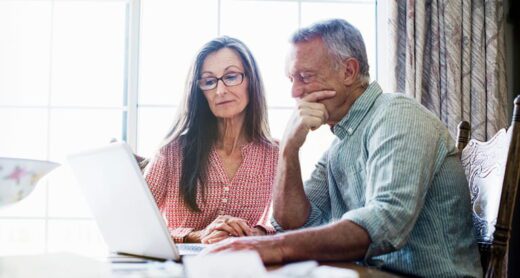 A retirement-aged man and woman review their financial accounts on a laptop computer.