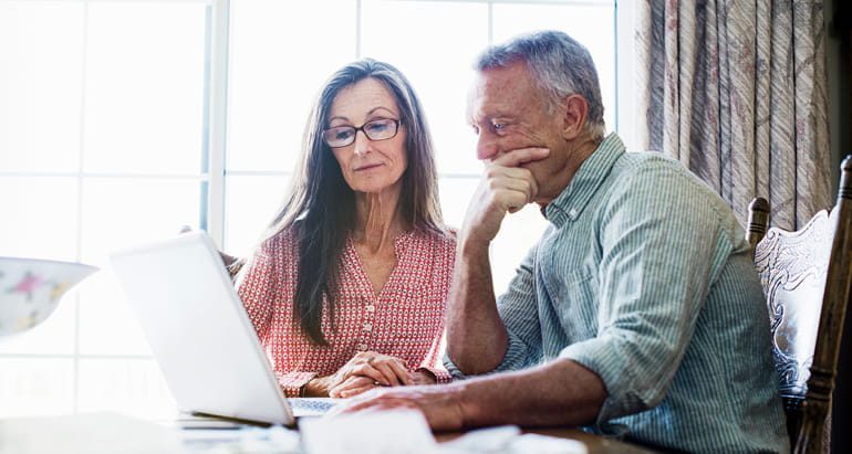A retirement-aged man and woman review their financial accounts on a laptop computer.