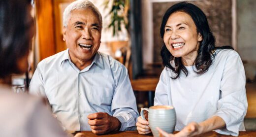 A happy couple discusses Medicare coverage options with an insurance agent over coffee in their home.