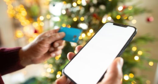 Close up of man's hand holding a smartphone and credit card near Christmas tree.