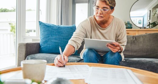 Shot of a mature woman using a digital tablet while going through paperwork at home.