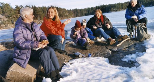 Multigenerational family resting on rocks on a lake in the winter.