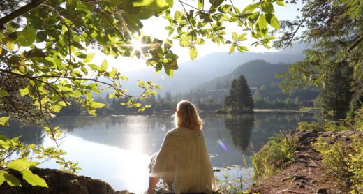 Woman relaxes on mountain lakeshore at sunrise.