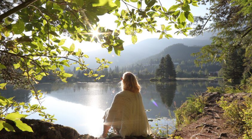 Woman relaxes on mountain lakeshore at sunrise.