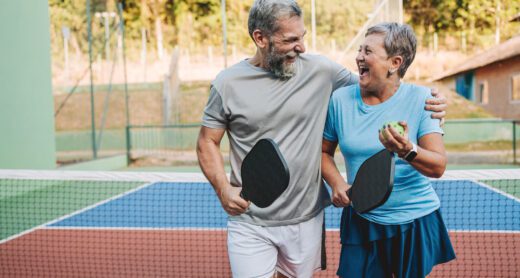 Senior couple on pickleball court, embracing while holding pickleball paddles.