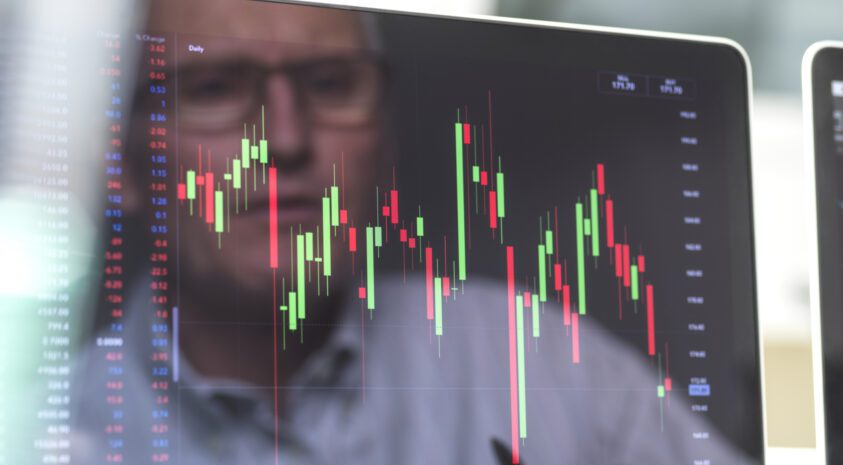 Middle aged man's face reflected in computer screen showing stock market investment graph.