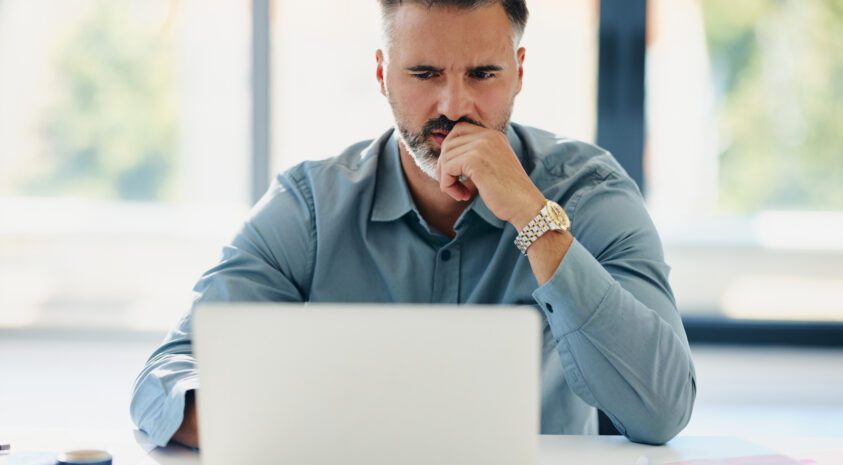 Thoughtful businessman working on laptop in the office.