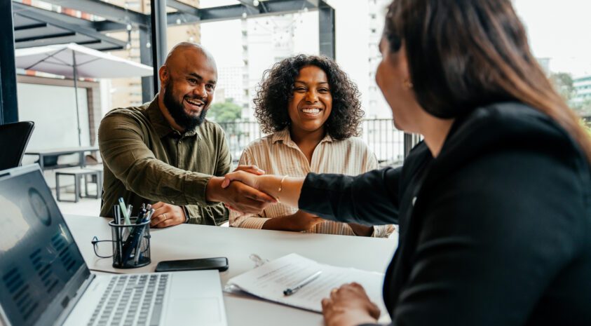 Middle aged couple smile and shake hands with a female financial professional.