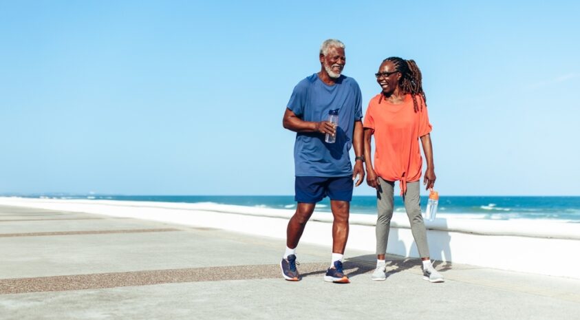 An elderly couple walks on a beach.