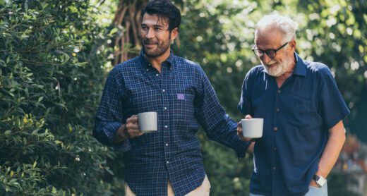 Adult son walking holding coffee mug with his father also holding a coffee mug.