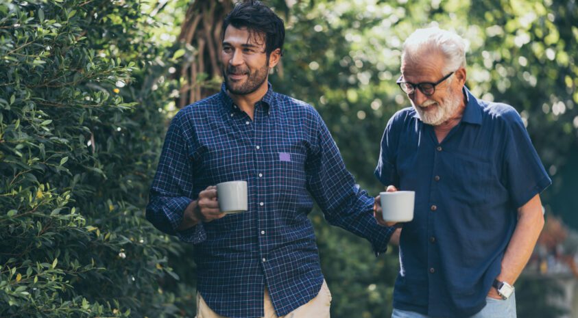 Adult son walking holding coffee mug with his father also holding a coffee mug.