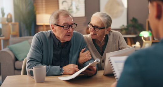 Older couple wearing glasses smiling at each other while going over paperwork with an advisor.
