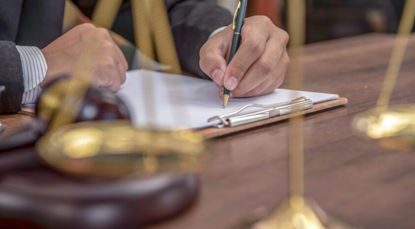 Close up of lawyer's hands signing papers in a courtroom setting.