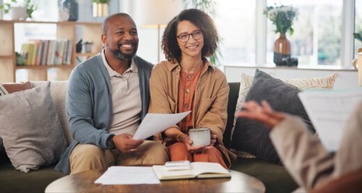 Middle aged couple smiling sitting on couch with a financial planner.
