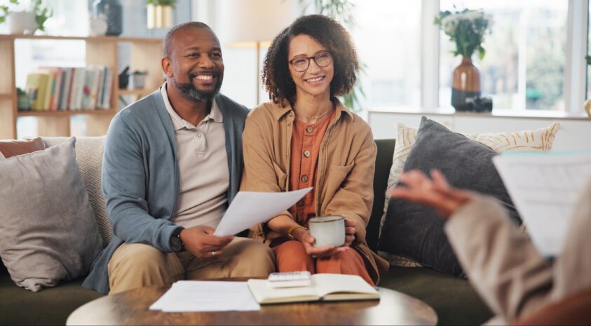 Middle aged couple smiling sitting on couch with a financial planner.